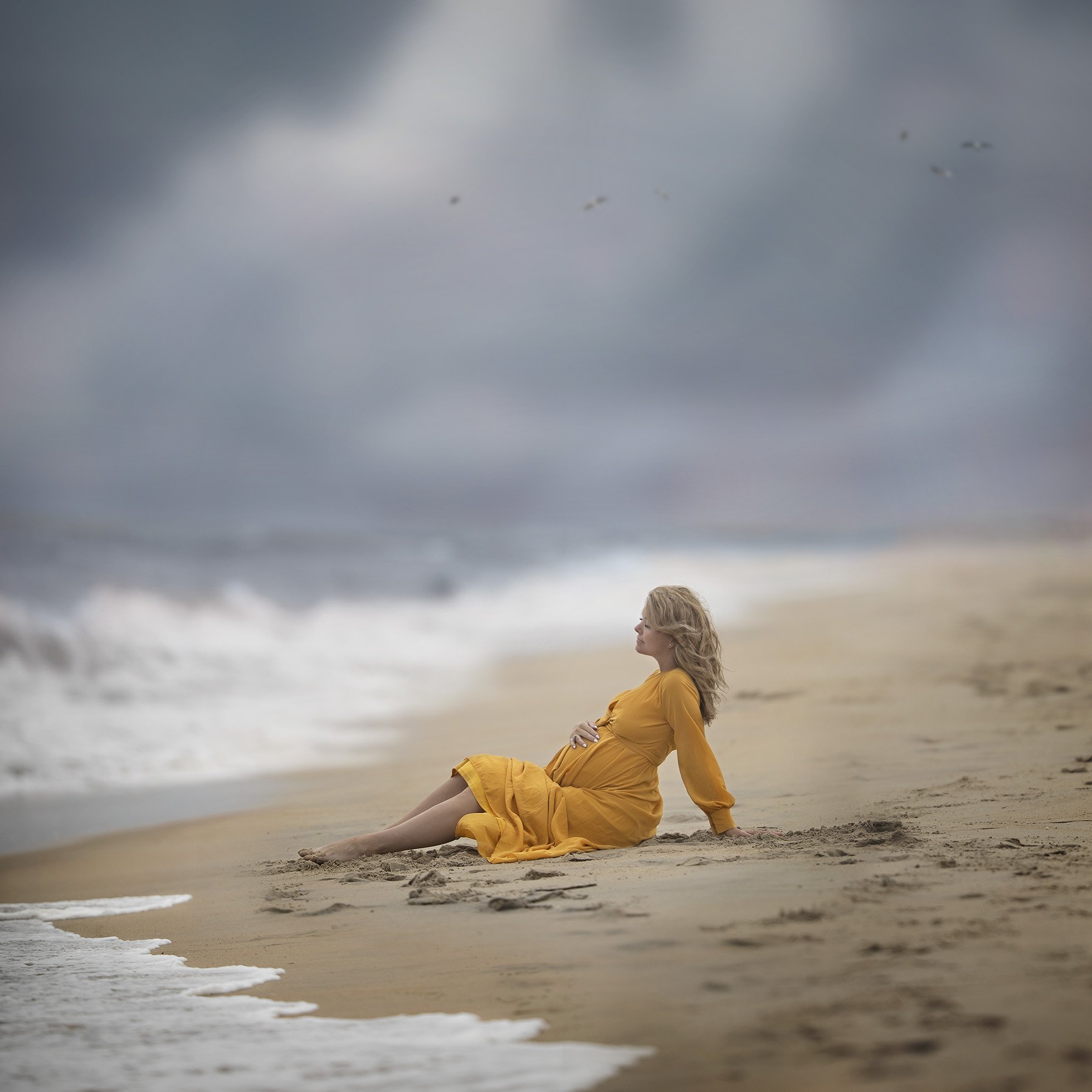 Pregnancy Self Portrait. Pregnant woman sitting on the beach.