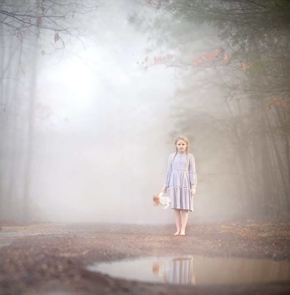 Spooky photo of a little girl in the fog with a doll.