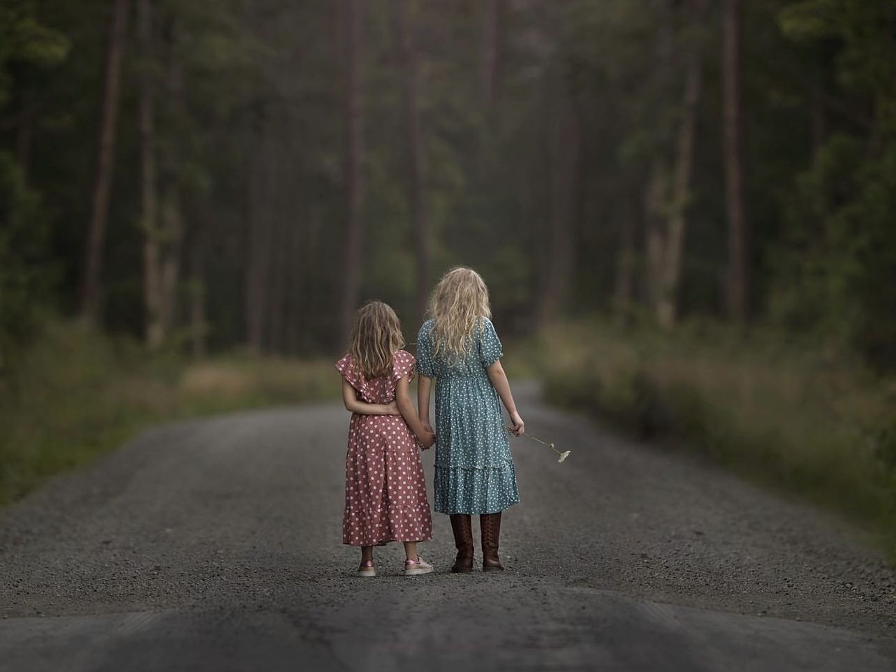 Two little girls hold hands as they walk down the road.
