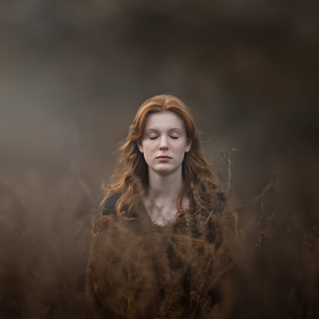 Winter Light Photography. Fine Art Portrait of red haired girl amongst brown winter foliage.