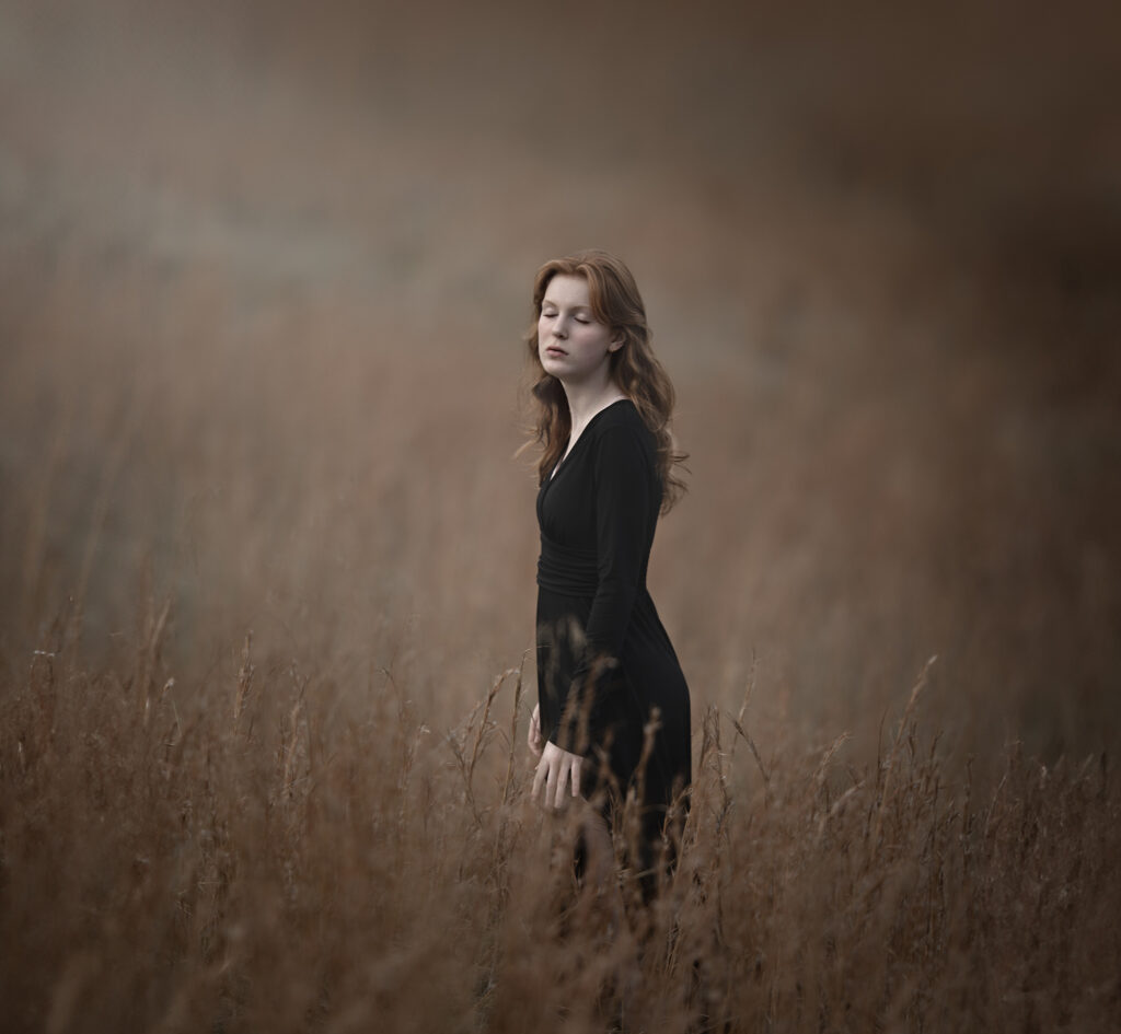Fine art photography portrait of a young woman in a black dress in a field
