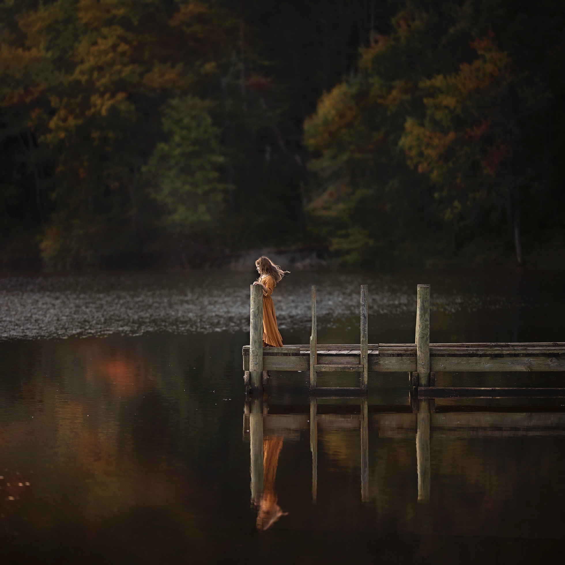 overcoming creative challenges. Girl standing on dock by a lake in the fall.