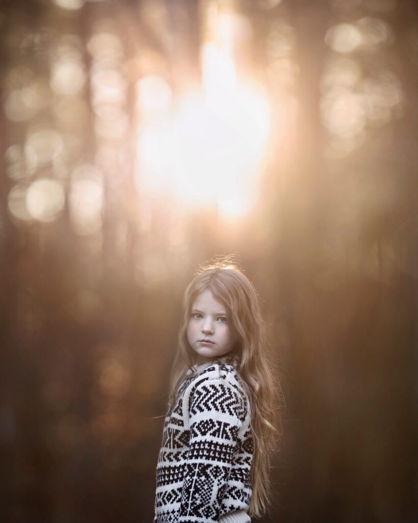 Winter Light Photgraphy. Girl standing infront of bare trees with light streaming.