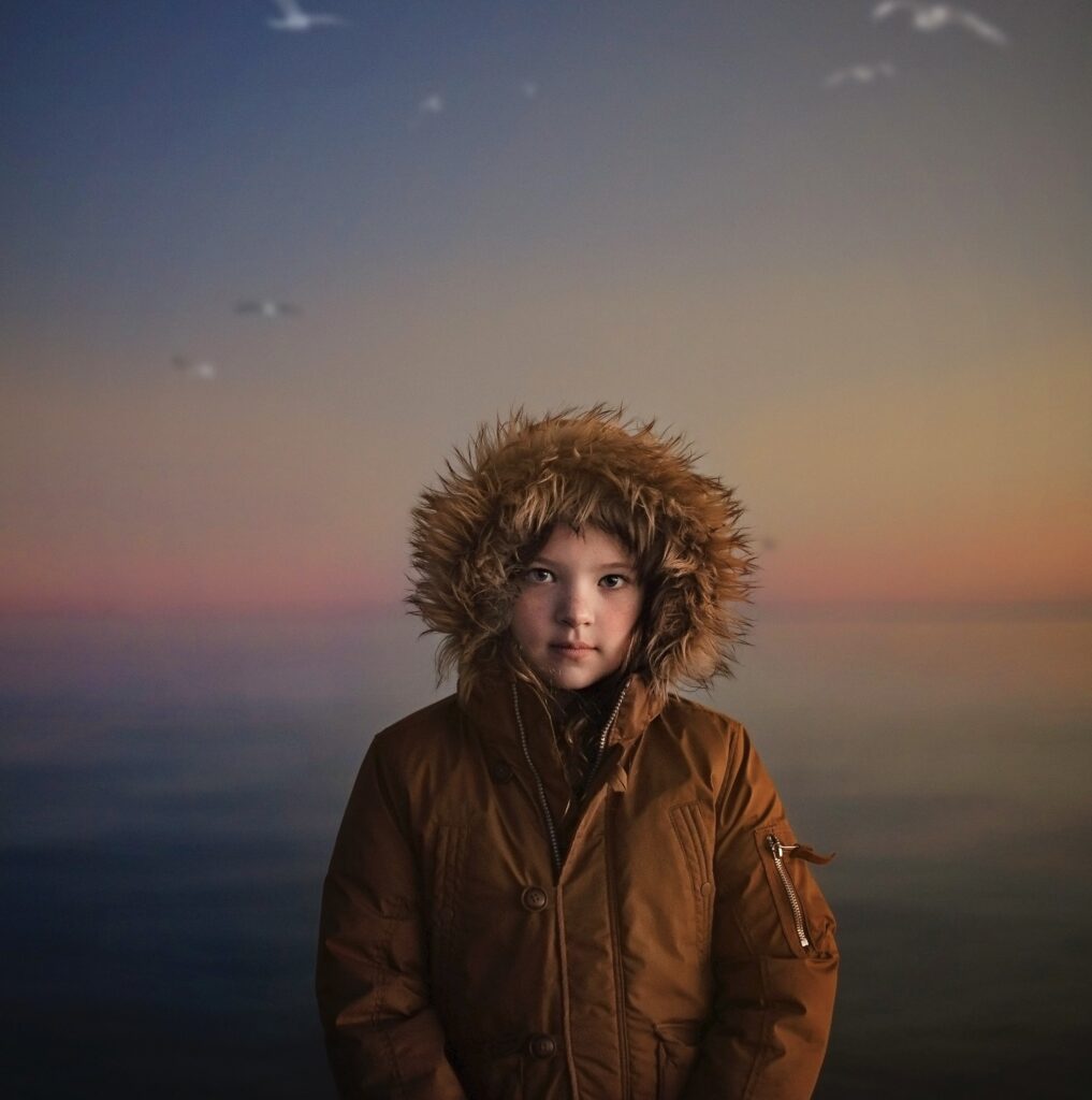 Winter Light Photography. Girl in coat standing on beach at sunrise in the Winter